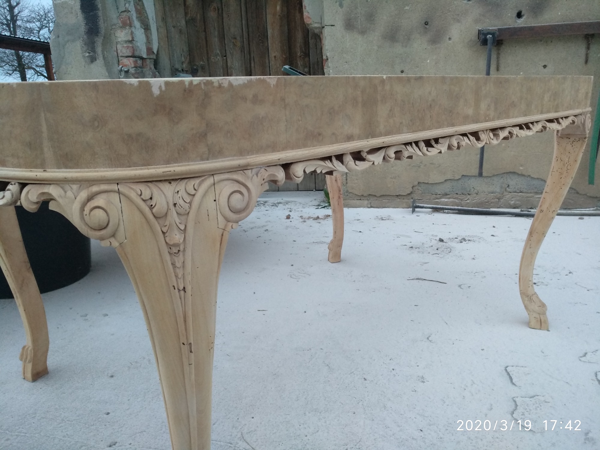 Stół z ozdobnymi nogami przed renowacją, widoczne ślady starej farby i zabrudzenia, przygotowany do dalszej obróbki.