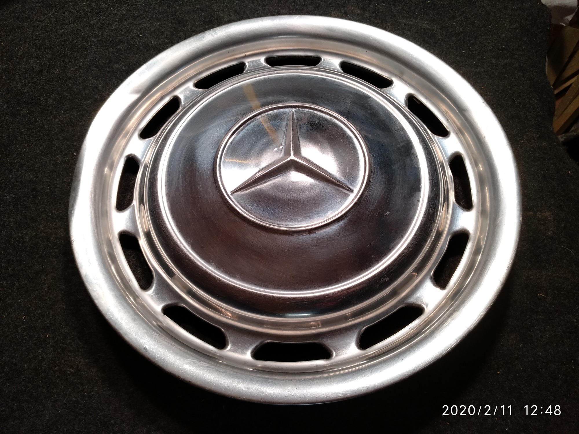 Wypolerowana, srebrna felga samochodowa Mercedes z widocznym logo na tle ciemnej, teksturowanej powierzchni.