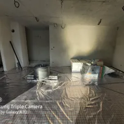 Rozłożona mata grzewcza pod ogrzewanie podłogowe w surowym wnętrzu, widoczne zwoje kabli grzewczych, materiały izolacyjne i narzędzia.