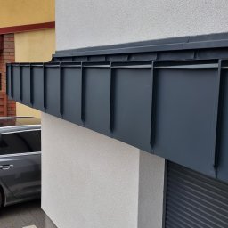 CuDACH Marcin Cuderski - Szare, metalowe orynnowanie dachu nowoczesnego budynku, widoczne z boku, z fragmentem zaparkowanego samochodu w tle.