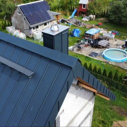 CuDACH Marcin Cuderski - Nowoczesny, grafitowy dach z blachy na domu jednorodzinnym, widok z góry. Na dachu zamontowany system odśnieżania. W tle dom z panelami słonecznymi i bałagan na podwórku.