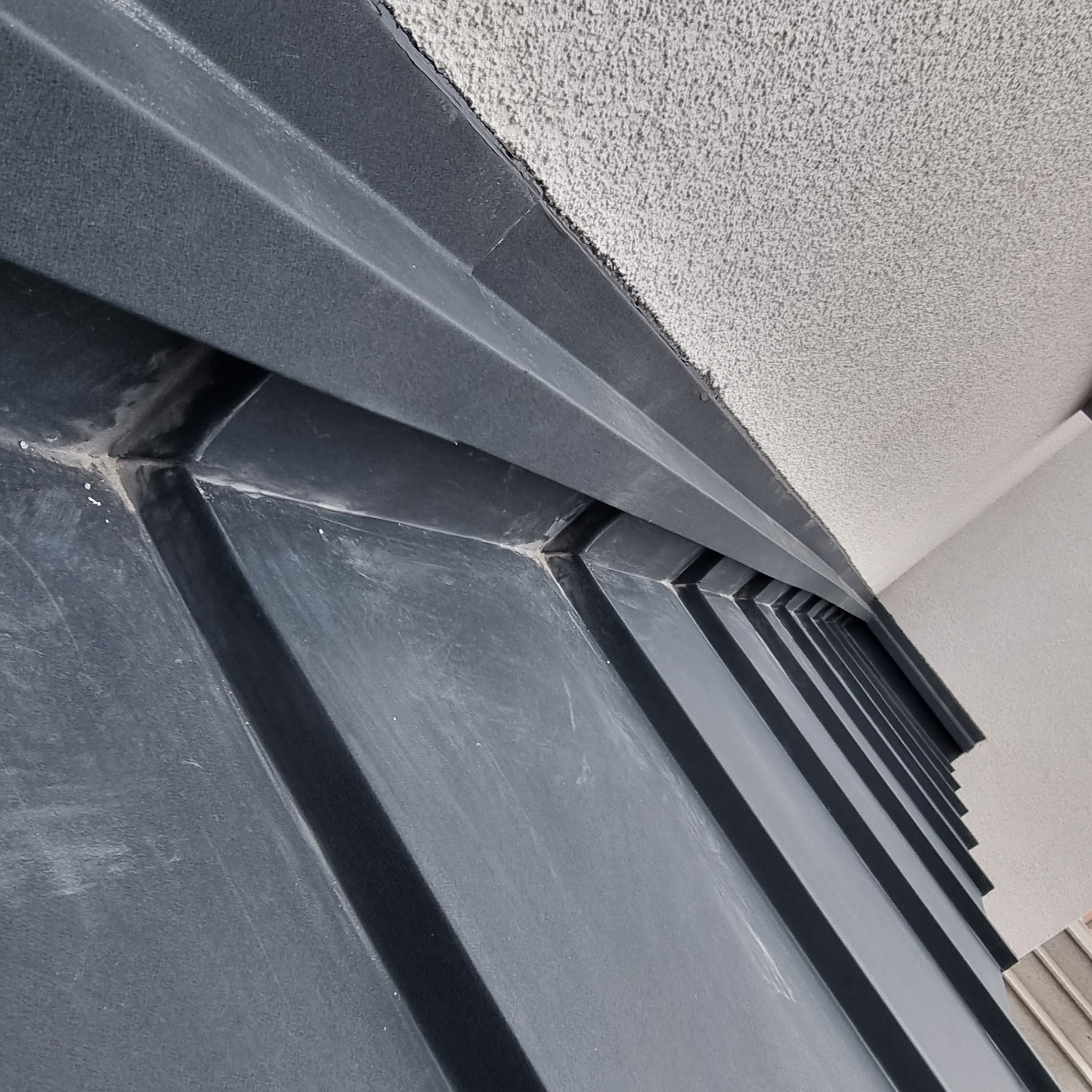 Szare panele blaszane na dachu, widok z dołu, detale łączeń i faktura materiału.