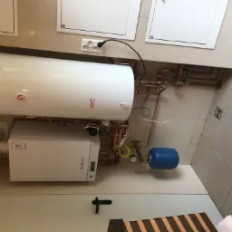 Kocioł gazowy Viessmann i biały zasobnik ciepłej wody Classic Spiro z widocznymi przyłączami miedzianymi w łazience z beżowymi płytkami.