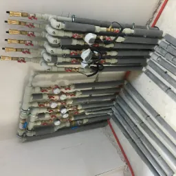 Rozbudowana instalacja wodna z licznymi zaworami, rurami z izolacją termiczną i wodomierzami, zamontowana przy suficie w surowym stanie wykończenia.