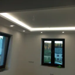 Nowoczesne oświetlenie sufitowe LED z listwą i punktowymi lampami w nowym, jeszcze nieumeblowanym pomieszczeniu z widokiem na las za oknem.