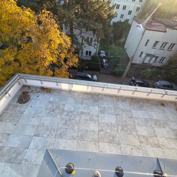 Roll and Wall Sebastian Ciszewski - Wykończony taras na dachu budynku z szarymi płytkami, widok z góry. Na płytkach leżą opadłe liście. W tle budynki mieszkalne i drzewa w jesiennej kolorystyce.