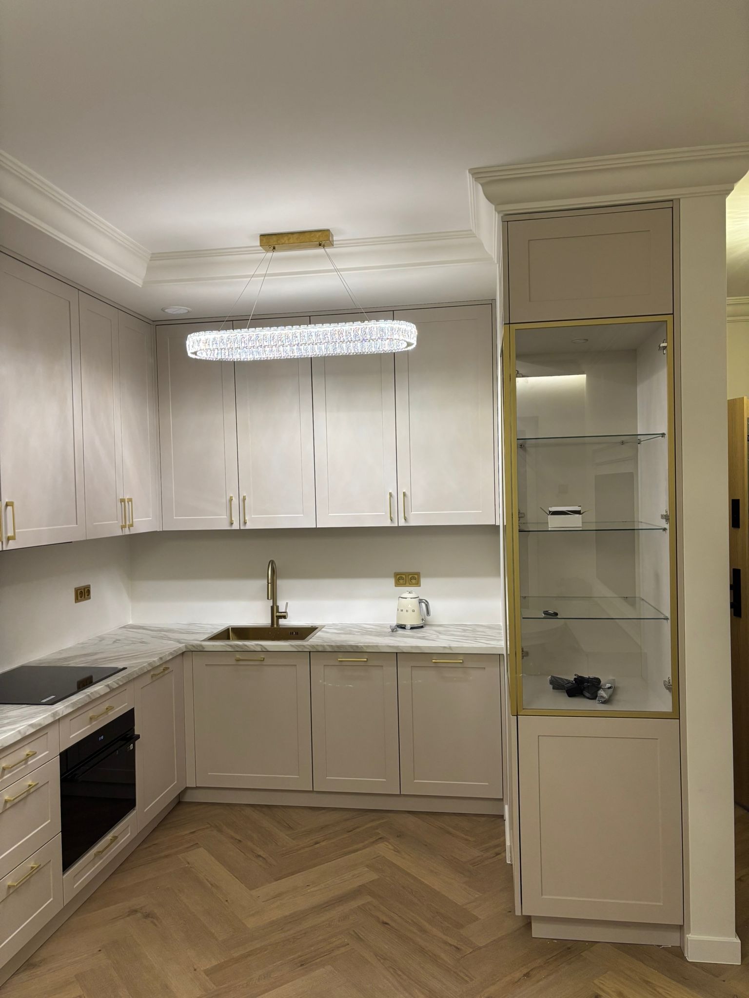 Elegancka kuchnia w odcieniach beżu z marmurowym blatem, złotymi akcentami i parkietem w jodełkę. Kryształowy żyrandol dodaje luksusowego charakteru.