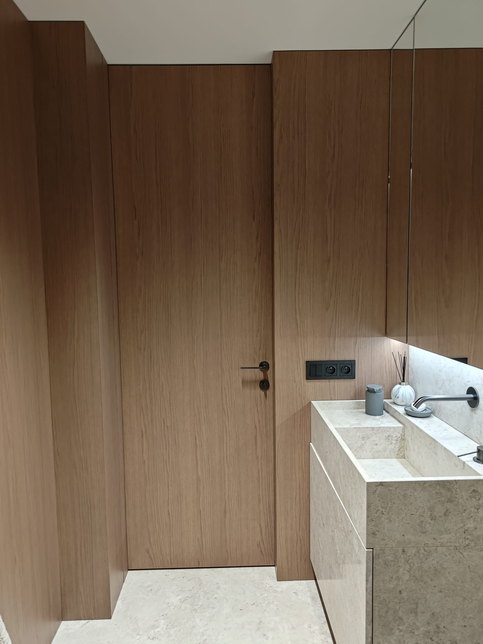 Nowoczesna łazienka z drewnianą zabudową, kamienną umywalką i minimalistyczną armaturą. Subtelne oświetlenie LED podkreśla elegancję wnętrza.