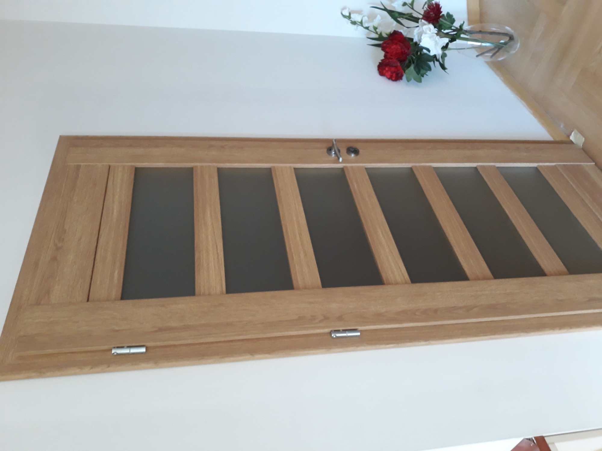 Drewniane drzwi wewnętrzne z przeszkleniami w pionowe pasy, zamontowane w białej ścianie, z dekoracyjnym bukietem kwiatów w tle.