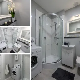 Nowoczesna łazienka w szaro-białej tonacji z kabiną prysznicową, pralką i umywalką z szafką, dopełniona dekoracjami jak storczyk w doniczce i świece.