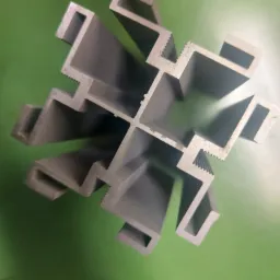 Szary aluminiowy profil o skomplikowanym przekroju poprzecznym, widoczne rowki i wypustki, ułożony na zielonym tle.