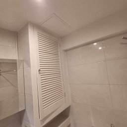 Roman Graczyk - Nowoczesna łazienka z zabudowaną szafką z lamelami, jasne płytki na ścianach i suficie, minimalistyczna armatura.