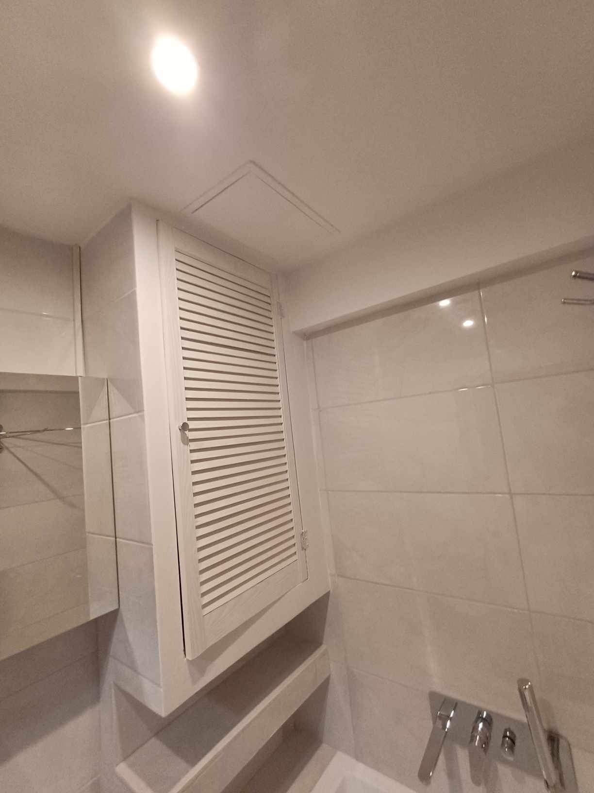 Nowoczesna łazienka z zabudowaną szafką z lamelami, jasne płytki na ścianach i suficie, minimalistyczna armatura.