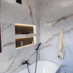 Nowoczesna łazienka z wanną, baterią w kolorze miedzi i marmurowymi płytkami z podświetlanymi wnękami, w których znajdują się dekoracje.