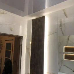 Nowoczesna łazienka z podświetlanym panelem dekoracyjnym i marmurowymi płytkami, widoczny fragment lustra i sufitu napinanego.