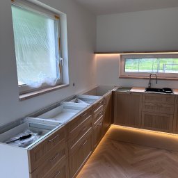 PT. LTD CONSTRUCTION - Montaż drewnianej zabudowy kuchennej z oświetleniem LED. Okno zabezpieczone folią. Parkiet ułożony w jodełkę. Częściowo zamontowane szafki z szufladami.