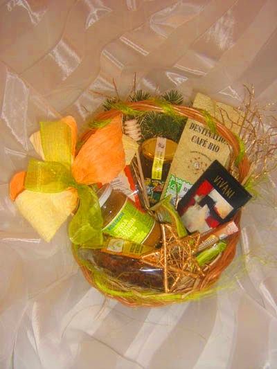 Koszyk prezentowy z kawą bio, miodem, konfiturami i ozdobnym pomarańczowo-żółtym kokardą na błyszczącym, kremowym tle.