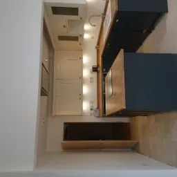 Nowoczesna aranżacja kuchni w Łomży: kremowe szafki z oświetleniem punktowym, ciemnogranatowa wyspa z drewnianym blatem i jasna, ceramiczna podłoga.