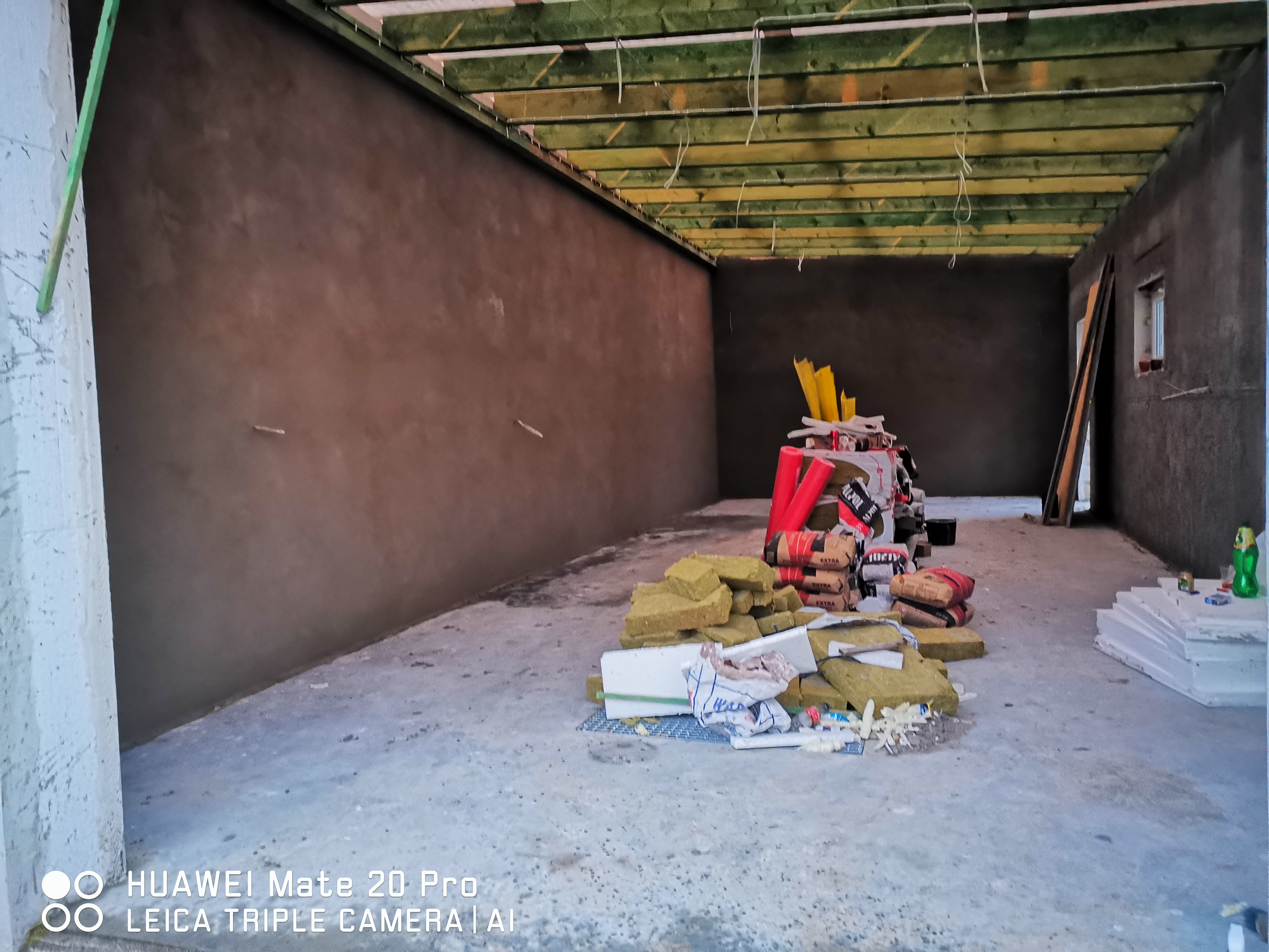 Wnętrze w trakcie ocieplania poddasza: widoczne drewniane belki stropowe, ocieplone ściany, materiały izolacyjne (wełna mineralna, styropian) oraz worki z zaprawą budowlaną