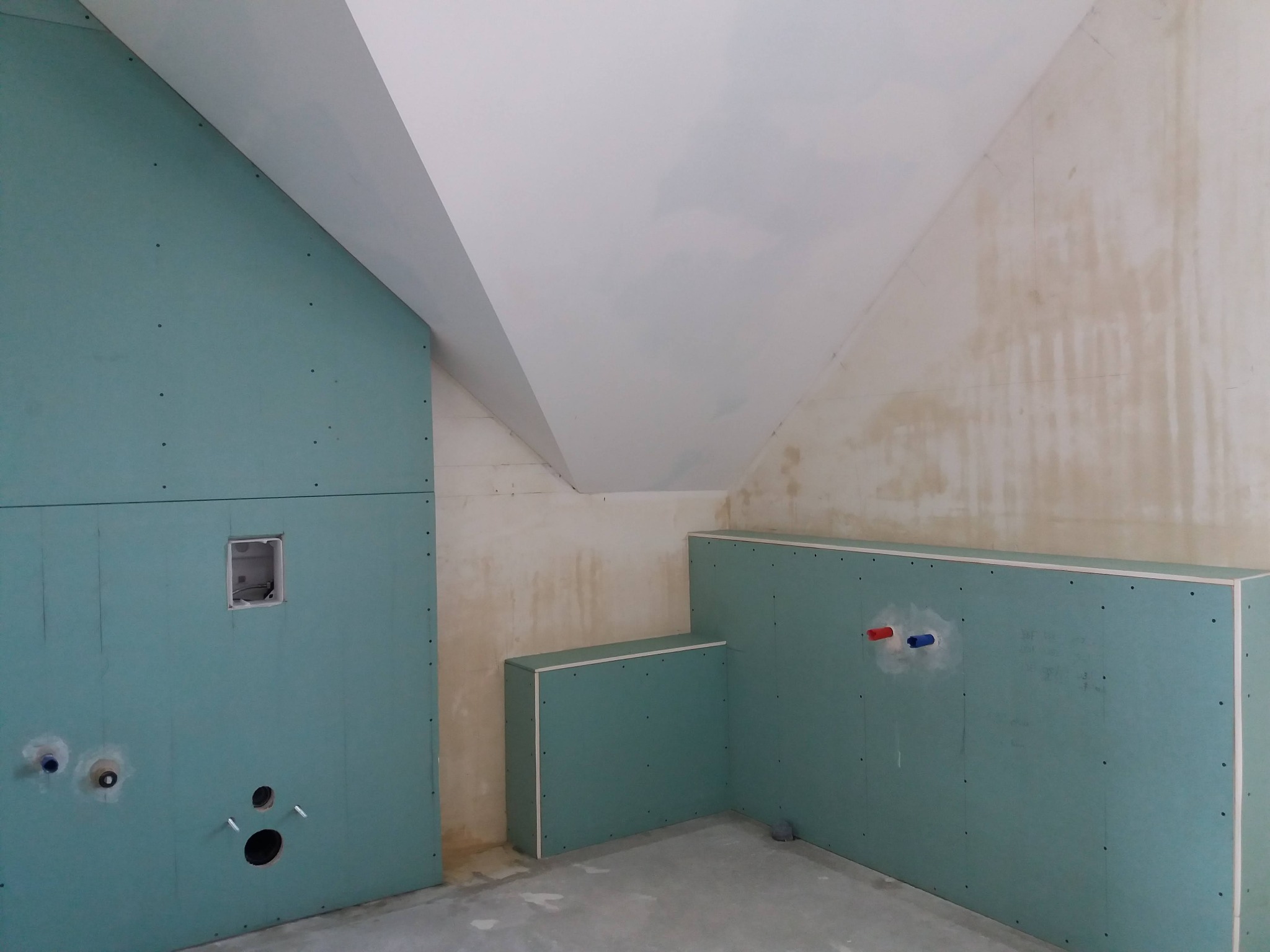 Ściany w łazience w trakcie montażu płyt kartonowo-gipsowych, widoczne otwory na instalacje i puszka elektryczna, surowy beton na podłodze.