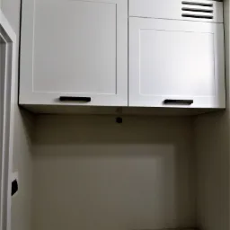 Białe szafki wiszące z czarnymi uchwytami nad umywalką w łazience, z widocznym fragmentem lampy sufitowej.