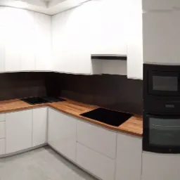 Nowoczesna kuchnia z białymi frontami i drewnianym blatem, czarne AGD w zabudowie, szara ściana nad blatem, widok na korytarz z narzędziami w tle.