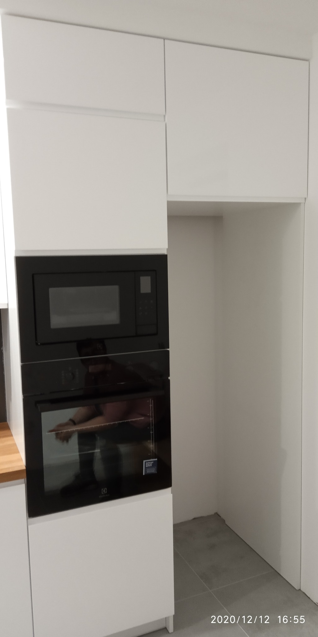 Biała zabudowa kuchenna z czarnym piekarnikiem i mikrofalówką, pusta wnęka obok, widoczna data i godzina wykonania zdjęcia.