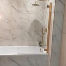 ANDRE - MONT Andrzej Strembicki - Biała wanna obłożona marmurowymi płytkami z złotą armaturą i szklanym parawanem.