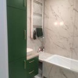 ANDRE - MONT Andrzej Strembicki - Nowoczesna łazienka z zielonymi szafkami, marmurowymi płytkami na ścianach i zabudowaną wanną. Biały grzejnik drabinkowy z czarnymi ręcznikami. Umywalka nablatowa z beżowym blatem.