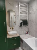 Nowoczesna łazienka z marmurowymi płytkami, owalnym lustrem z podświetleniem, zielonymi szafkami i grzejnikiem drabinkowym z ręcznikiem.