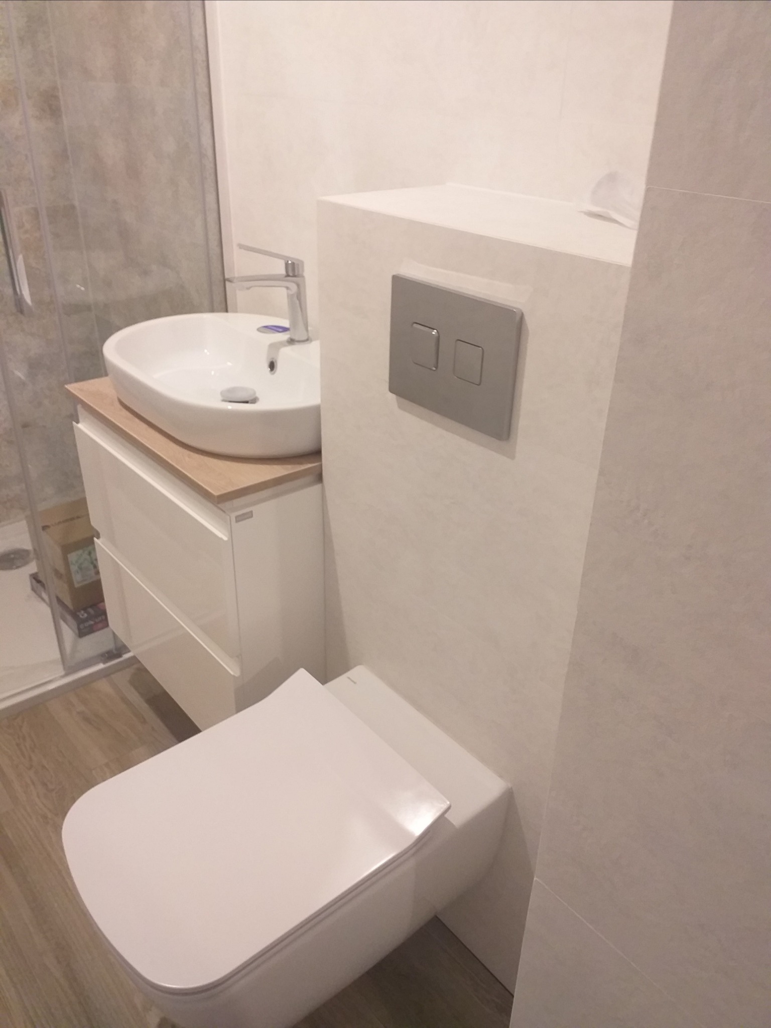 Nowoczesna łazienka z podwieszaną miską WC, umywalką nablatową na szafce z drewnianym blatem i szarą płytką imitującą kamień na ścianach.