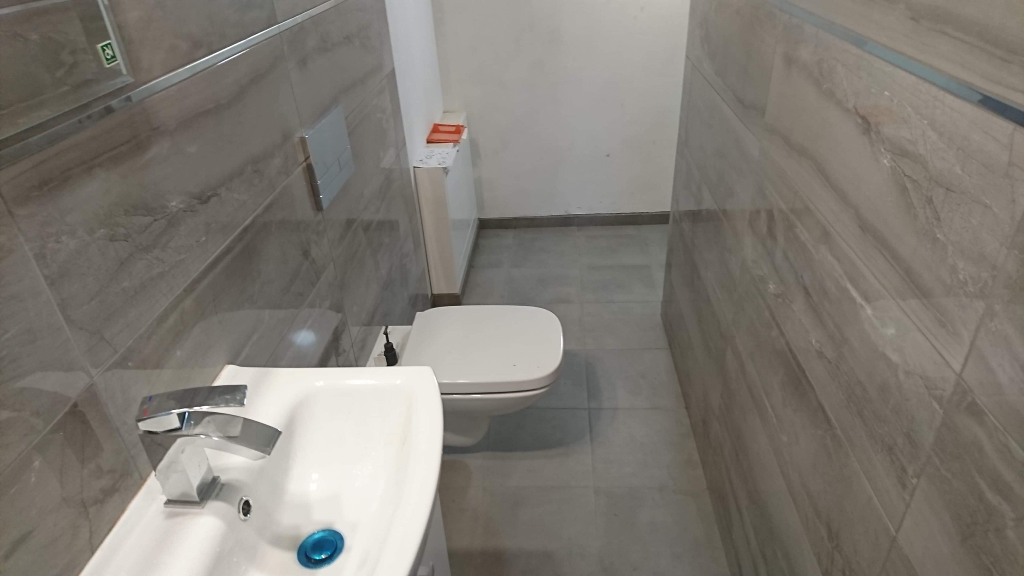 Ukończona łazienka z toaletą, umywalką z chromowaną baterią i szarymi płytkami imitującymi marmur na ścianach i podłodze.