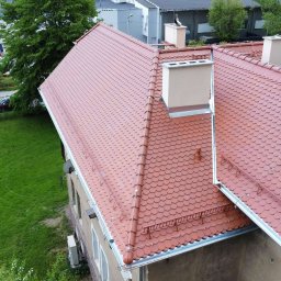 „BUD” Borucki Usługi Dekarskie Piotr Borucki - Czerwony dach z dachówki karpiówki, widok z góry na budynek z trawnikiem i parkingiem w tle. Widoczne kominy i metalowe obróbki blacharskie.