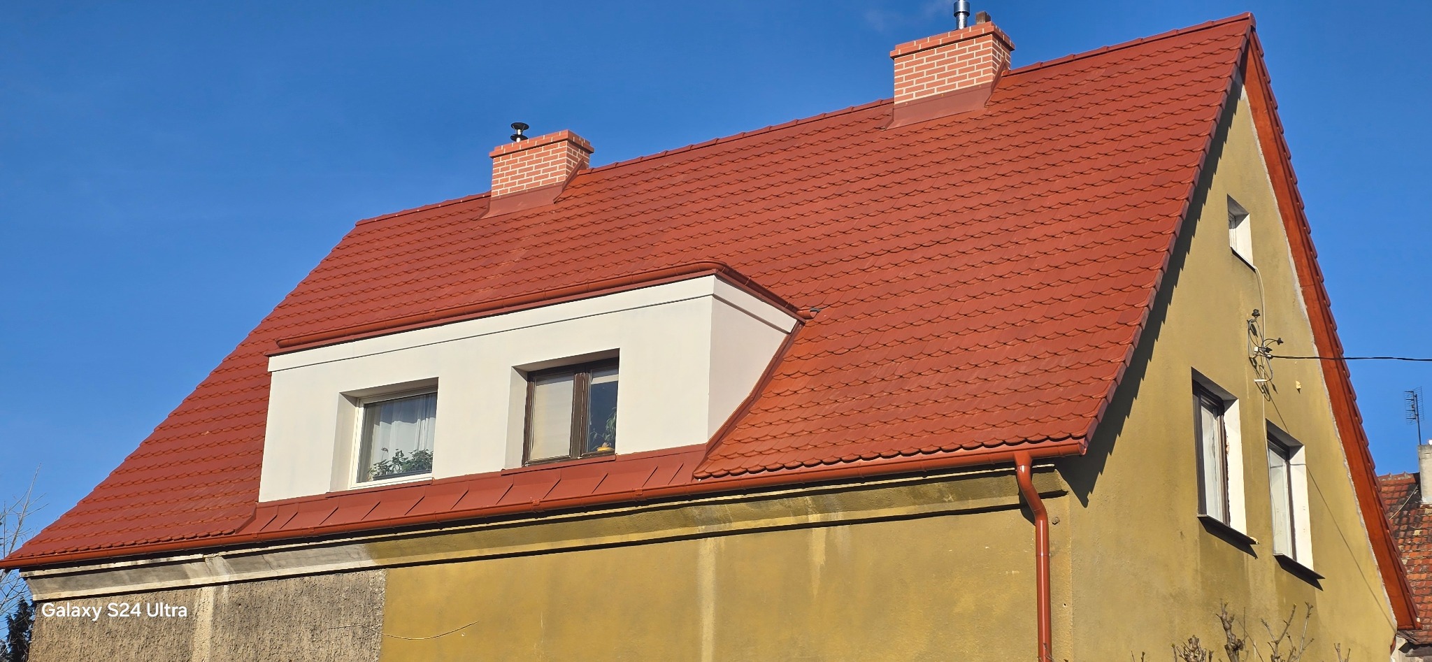 Dom z nowym dachem z czerwonej dachówki karpiówki, widoczny komin z cegły klinkierowej i okna w lukarnie