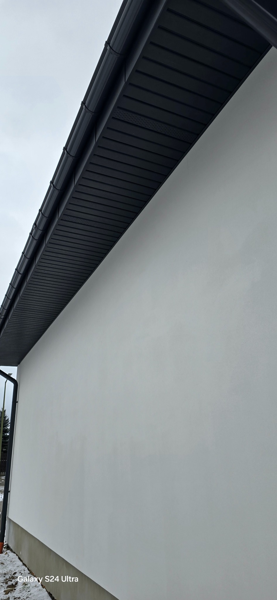 Nowoczesne, czarne orynnowanie i podbitka dachu kontrastujące z białą elewacją budynku, widok z dołu.