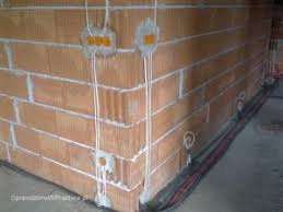 Instalacja elektryczna w nowo wznoszonym murze z pustaków ceramicznych, widoczne puszki instalacyjne i przewody wyprowadzone ze ściany.