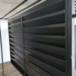 Nowoczesne, metalowe ogrodzenie lamelowe w kolorze grafitowym, zawieszone na metalowym stelażu w hali produkcyjnej przed montażem.