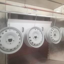 Prasmet Bieniek i Koniarczyk Sp.J - Cztery metalowe felgi samochodowe zawieszone na hakach w kabinie lakierniczej, po nałożeniu białej farby proszkowej.