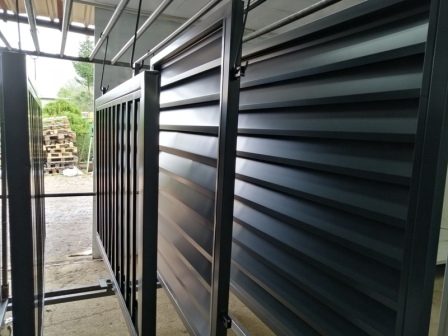 Elementy metalowe bramy przesuwnej z poziomymi lamelami zawieszone na wieszakach przygotowane do transportu lub dalszej obróbki.