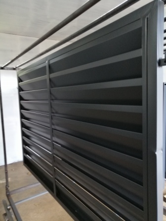 Nowoczesne, metalowe ogrodzenie lamelowe w kolorze grafitowym, zawieszone na metalowym stelażu w hali produkcyjnej przed montażem.