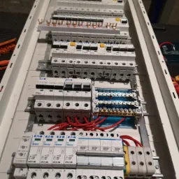 Rozdzielnica elektryczna z zamontowanymi bezpiecznikami i przewodami, widoczne marki Eaton i Hager, w trakcie podłączania.