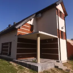 Dwukondygnacyjny dom z kremową elewacją i elementami z ciemnego drewna, widoczna klimatyzacja na ścianie, oświetlenie zewnętrzne i częściowo zadaszony taras z kolumną.