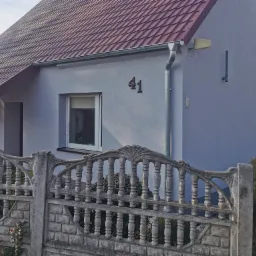 Dom jednorodzinny po ociepleniu elewacji, widoczny numer domu '41' i fragment dekoracyjnego betonowego ogrodzenia, antena satelitarna na ścianie.