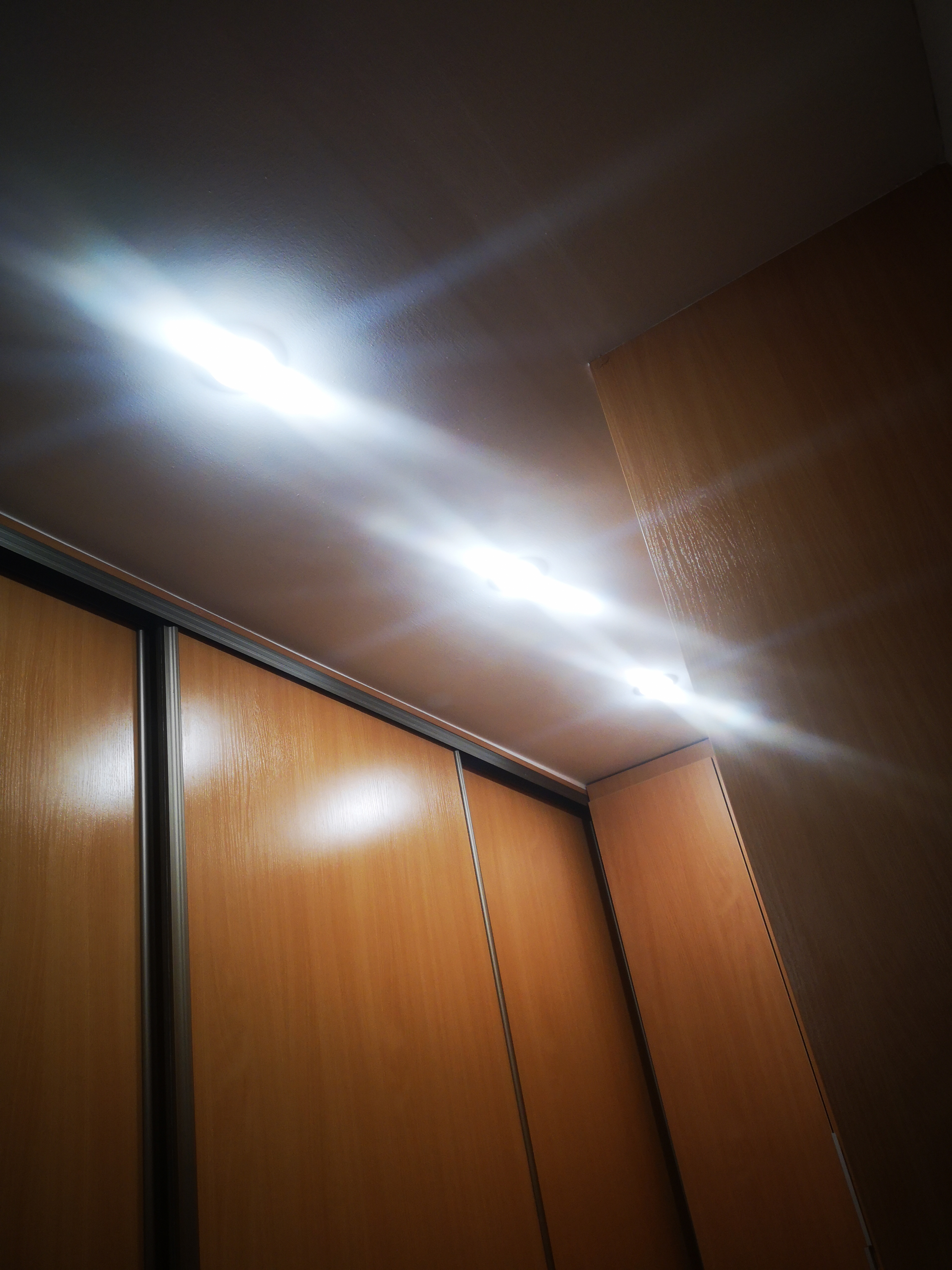 Wnętrze szafy przesuwnej z oświetleniem LED zamontowanym pod sufitem, widoczne z dołu pod kątem.