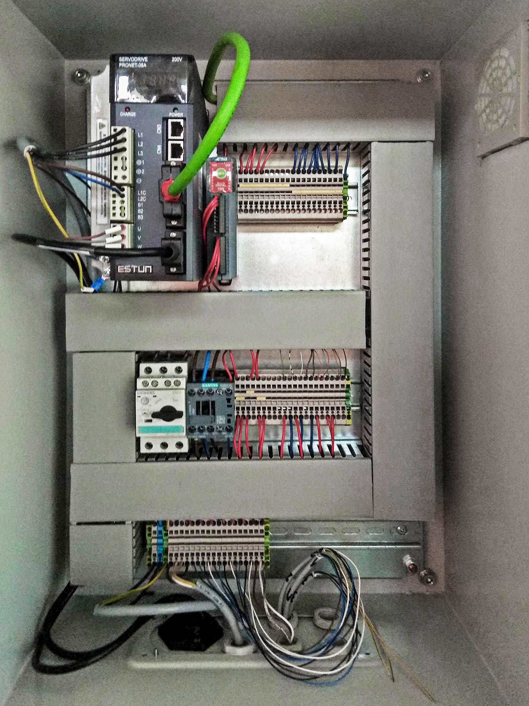 Wnętrze szarej szafy sterowniczej z widocznym serwonapędem ESTUN, modułami Siemens, licznymi przewodami i złączkami elektrycznymi. Zielony kabel biegnie od góry do serwonapędu.