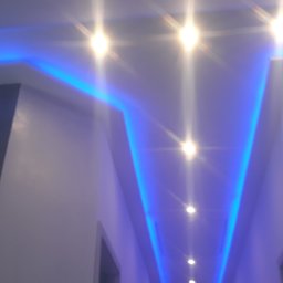 Wikrem - Nowoczesne oświetlenie sufitowe z niebieskimi listwami LED wzdłuż krawędzi, tworzące efektowny wizualnie korytarz z jasnymi punktowymi lampami.