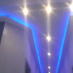 Nowoczesne oświetlenie sufitowe z niebieskimi listwami LED wzdłuż krawędzi, tworzące efektowny wizualnie korytarz z jasnymi punktowymi lampami.