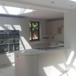 Wikrem - Jasna kuchnia w trakcie remontu, z czterema piekarnikami w zabudowie, wyspą kuchenną i oknem dachowym wpuszczającym promienie słoneczne.