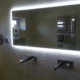 Wikrem - Nowoczesna łazienka w Szewcach po remoncie: podświetlane lustro, armatura podtynkowa i grzejnik drabinkowy na tle beżowych płytek z delikatną fakturą.