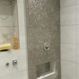 Wikrem - Ściana prysznicowa wyłożona mozaiką z wnękami na kosmetyki, widoczny zawór sterujący i fragment poziomicy na podłodze, w trakcie prac wykończeniowych.